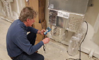 Man installing foil insulation on pipes in a basement.